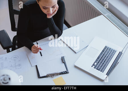 Draufsicht der Frau, die Analyse der Geschäftsentwicklung in einem Diagramm beim Sitzen an ihrem Schreibtisch im Büro. Stockfoto