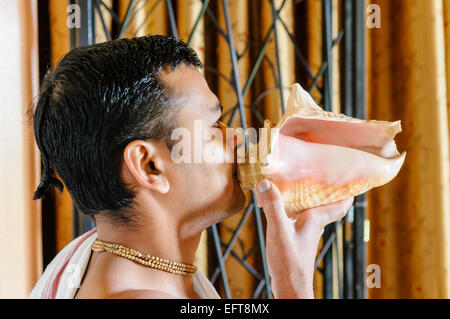 Ein Hare-Krishna-Anhänger bläst in ein Horn im Rahmen einer Feierstunde einen Ton erzeugen. Stockfoto