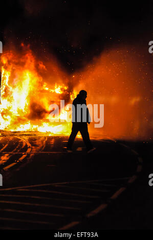 Ein Mann geht vor einem brennenden Bus nach zwingt den Fahrer ab und setzten es in Brand. Stockfoto
