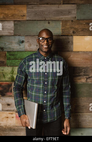 Porträt von zuversichtlich junger Geschäftsmann lächelnd gegen Holzwand im Büro Stockfoto
