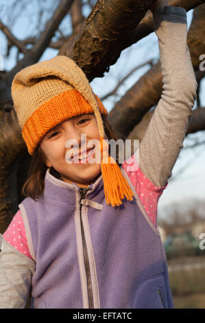 Junges Mädchen schwingen auf einem Ast im Herbst tragen gestrickte Zipfelmütze. Stockfoto