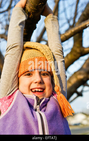 Junges Mädchen schwingen auf einem Ast im Herbst tragen gestrickte Zipfelmütze. Stockfoto