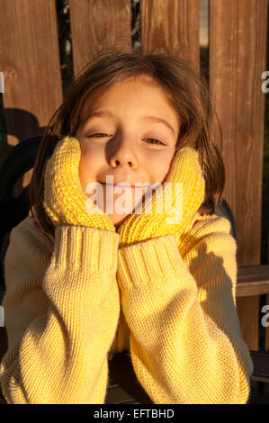 Junges Mädchen mit einem dummen Lächeln tragen gelbe Strickhandschuhe und gelbe Strickpullover. Stockfoto