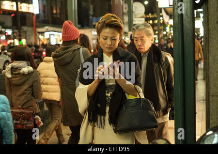 Auf ihrem Smartphone in der belebten shopping Bezirk Shijo Kawaramachi gekleidete Frau im Kimono. Kyoto, Japan. Stockfoto