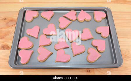 Backblech Herzform Cookies mit rosa Zuckerguss auf einem Holztisch Stockfoto