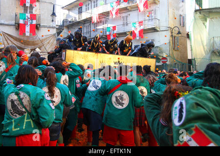 Ein Cart geht durch die engen Gassen der Altstadt, wie andere Teams werfen Orangen Ivrea Karnevalszeit umgeben Stockfoto