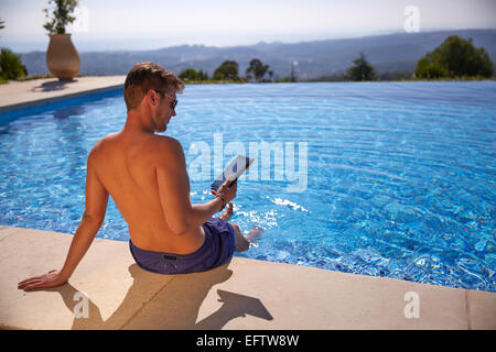 Junger Mann am Pool im Urlaub mit einem Tabletcomputer Stockfoto