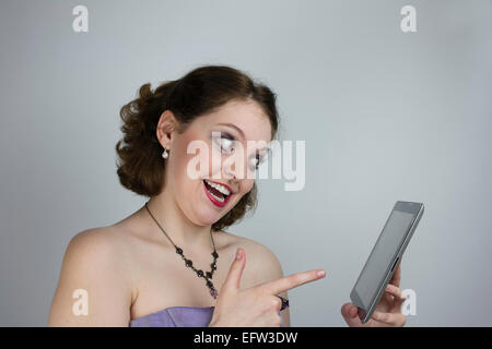 Glückliche junge Frau trägt lila Kleid und Strass Halskette mit Tablet. Stockfoto