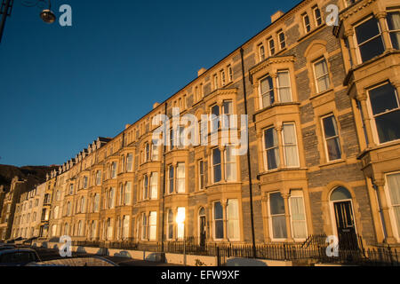 Reihenhäuser entlang der Victoria Terrasse, mit Blick auf Strand und Cardigan Bay bei Sonnenuntergang, Ceredigion, Mid Wales, Aberystwyth, Wales. Stockfoto