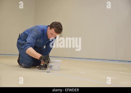 Ein Kaufmann malt den Rand der Bodenlinie bevor Epoxy Produkt in einem Industriegebäude verwendet wird Stockfoto