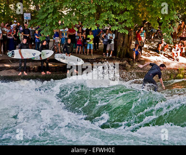 Die Menschen genießen eine touristische Attraktion in München, Surfer auf der künstlichen Welle am Eisbach, kleinen Fluss über die Englis Stockfoto