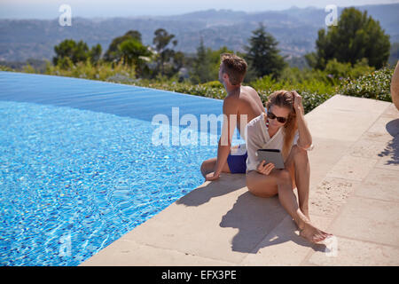 Junges Paar sitzt am Pool im Urlaub in Südfrankreich mit der Frau mit einem tablet Stockfoto