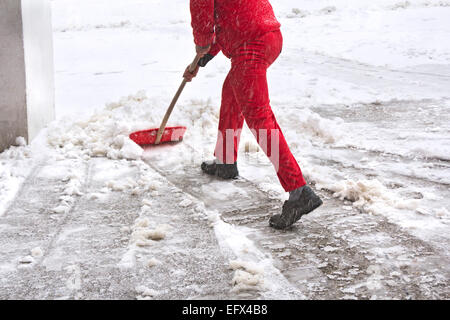 Arbeiter in roten Uniform entfernt Schnee mit roten Schaufel Stockfoto