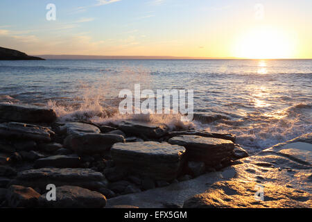 Wellen brechen in der Abenddämmerung über Felsen am walisischen Strand. Stockfoto