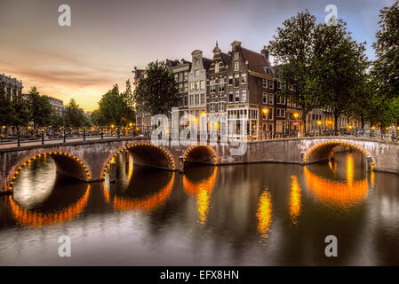 Beleuchtete Bogenbrücken gegossen leuchtende Reflexionen auf den Grachten in Amsterdam, Niederlande-Hervorhebung der markanten Architektur Stockfoto