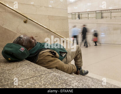 New York, NY - 28. Januar 2015 Obdachloser auf Treppen in Grand Central Station, New York mit Menschen zu Fuß durch Stockfoto