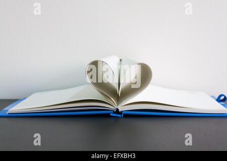 Seiten eines Buches in Form eines Herzens auf Tisch gebogen Stockfoto