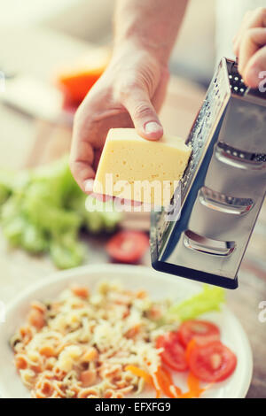 Nahaufnahme von männlichen Händen reiben von Käse über Nudeln Stockfoto