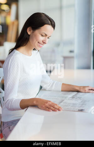 lächelnde junge Frau lesen Zeitung im café Stockfoto