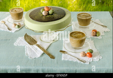 Ostertisch mit Tee Matcha Käsekuchen und weißen Kaffee auf Hintergrund von grünem Rasen Stockfoto