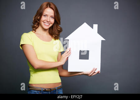 Glückliche junge Frau zeigt Papierhaus Stockfoto