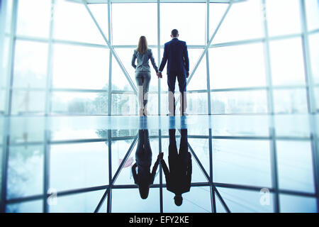 Junger Mann und Frau in festlich gekleidet, hält mit den Händen stehend durch Bürofenster Stockfoto