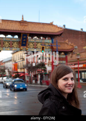 Eine hübsche Brünette Mädchen vor das Tor der harmonischen Interesse in Chinatown, Victoria, Britisch-Kolumbien, Kanada. Stockfoto