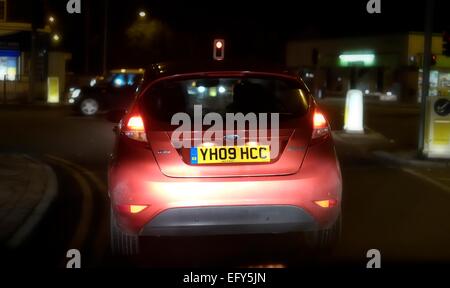 Ein Ford Fiesta warten an einer Straßenkreuzung, beleuchtet von den Scheinwerfern aus dem Auto hinter England UK Stockfoto
