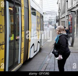 Eine Frau wartet auf die Straße zu überqueren, während ein Nottingham express Transit Straßenbahn vorbeifährt. England-UK Stockfoto