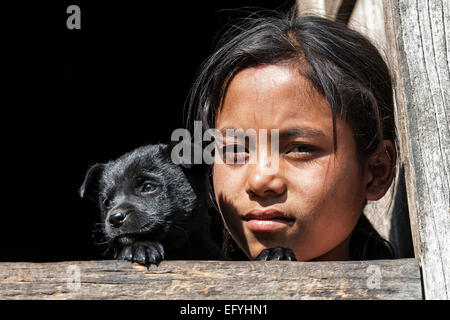 Nepalesische Mädchen mit einem Hund suchen, der aus einem Fenster, Porträt, in der Nähe von Panauti, Nepal Stockfoto