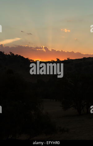 Eine unbearbeitete (RAW)-Foto auf den Sonnenuntergang hinter einigen Hügeln. Die untergehende Sonne ist durch einige tiefe Wolken verdeckt. Stockfoto