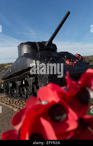 Aus Fokus rote Mohnblumen mit ein Sherman-Panzer-Denkmal im Hintergrund. Stockfoto