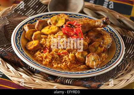 Jollof Reis mit gebratenem Huhn und Wegerich. Stockfoto