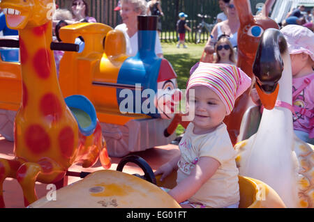 Lächelndes Mädchen Kleinkind genießt eine Fahrt auf einem Kinderlustig gehen rund Vergnügungsfahrt in einem lokalen Dorf Fete. Hempstead Kent Großbritannien Stockfoto