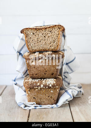 Vertikale Foto von einem Stapel von drei hausgemachten Vollkorn Roggen-Weizen Sauerteig Brot mit Samen auf einem klaren hölzernen Hintergrund gemischt. Stockfoto