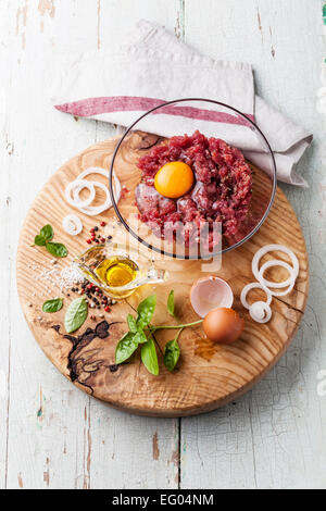 Frisches Hackfleisch mit Zwiebeln und Gewürzen in Schüssel auf Holzbrett auf blauem Hintergrund Stockfoto