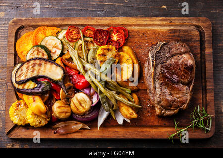 Club-Rindersteak und gegrilltes Gemüse auf Schneidebrett auf dunklem Holz Stockfoto