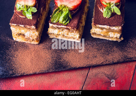 Drei tiramisu Kuchen auf schwarzem Schiefer und roten Holz- Hintergrund Stockfoto