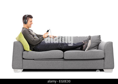 Junger Kerl liegt auf Sofa und anhören von Musik auf seinem Handy isoliert auf weißem Hintergrund Stockfoto