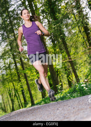Foto einer jungen Frau, Joggen und trainieren auf einem Schotterweg durch den Wald. Leichte Bewegungsunschärfe auf Jogger. Stockfoto