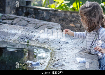 Mädchen Segeln Papierschiffchen in Brunnen Stockfoto