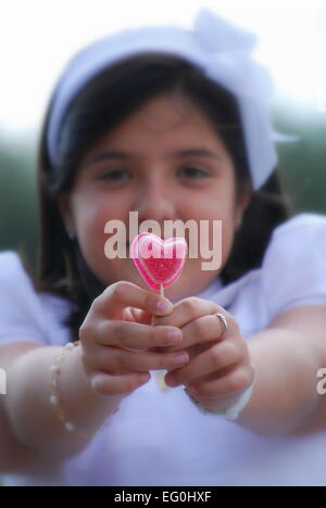 Porträt eines lächelnden Mädchens, das einen herzförmigen Gummy Lutscher hält Stockfoto