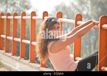 Langhaarige Frau stützte sich auf orange Barriere und lächelnd zu Kamera Stockfoto