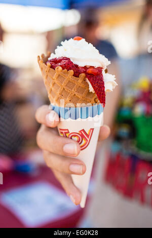 Frau Hand hält Eis-Kegel mit Erdbeeren und Sahne Stockfoto