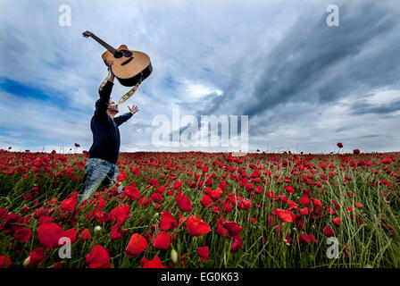 Mann mit Akustikgitarre im Mohnfeld Stockfoto