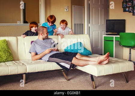 Drei jungen herausspringende hinter einem Sofa, ihren Vater zu überraschen Stockfoto