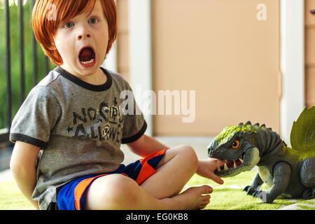 Jungen spielen mit Spielzeug Dinosaurier, so zu tun, er gebissen worden ist Stockfoto