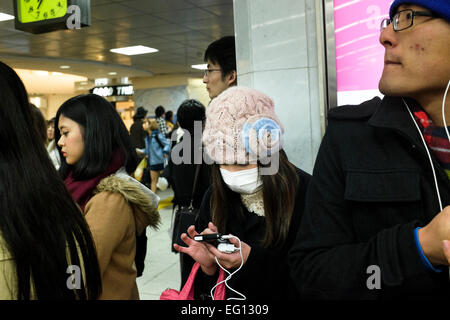 Pendler auf ihrem smart Phone tragen einen Mundschutz im Bahnhof Shinjuku. Shinjuku ist von 3,64 Millionen Fahrgäste pro Tag, so dass es den verkehrsreichsten Verkehrsknotenpunkt in der Welt verwendet. Tokio, Japan. Stockfoto