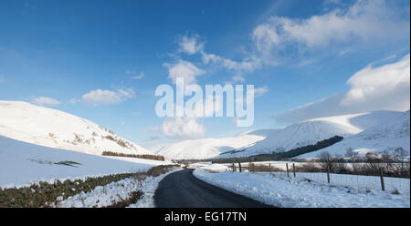 Leere Straße durch Schnee beklebt Hügel im Winter. Peebleshire, Scottish Borders, Schottland Stockfoto