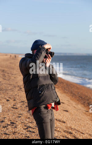 Junger Mann tragen 'Puffa' Jacke und wollene Mütze im Winter mit dem Fotografieren mit einer 35mm Kamera. Stockfoto